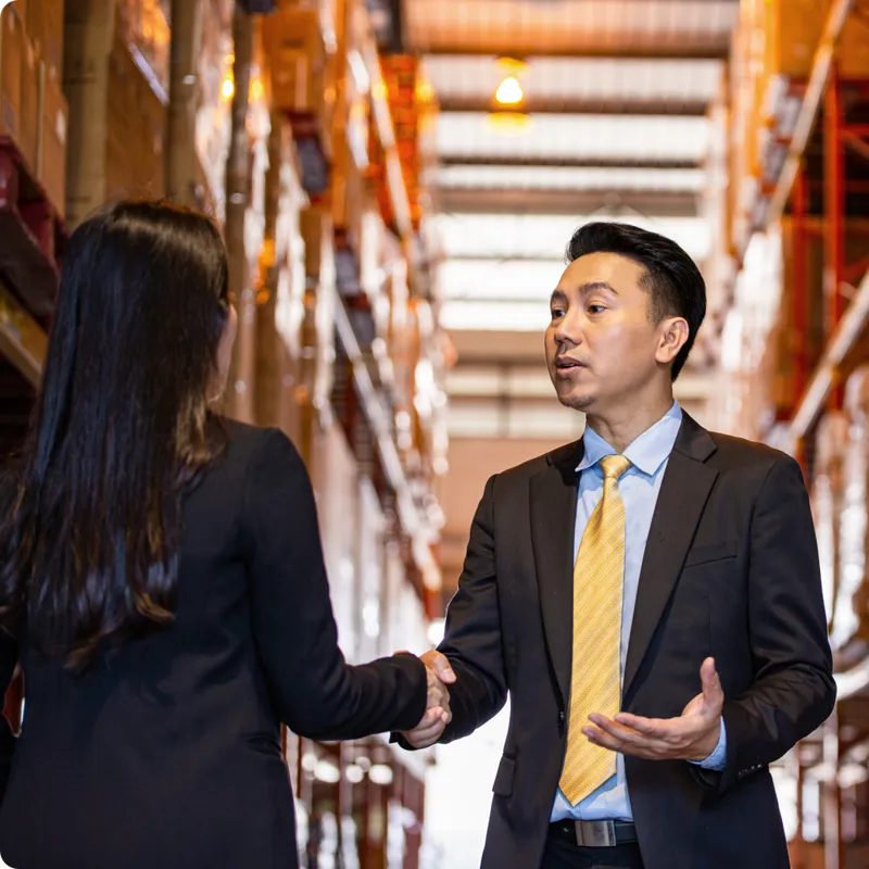 Professionals in a warehouse shake hands.