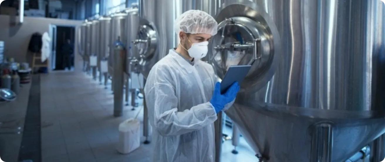 Factory worker wearing safety gloves, mask and hair net,  checking a computer tablet.