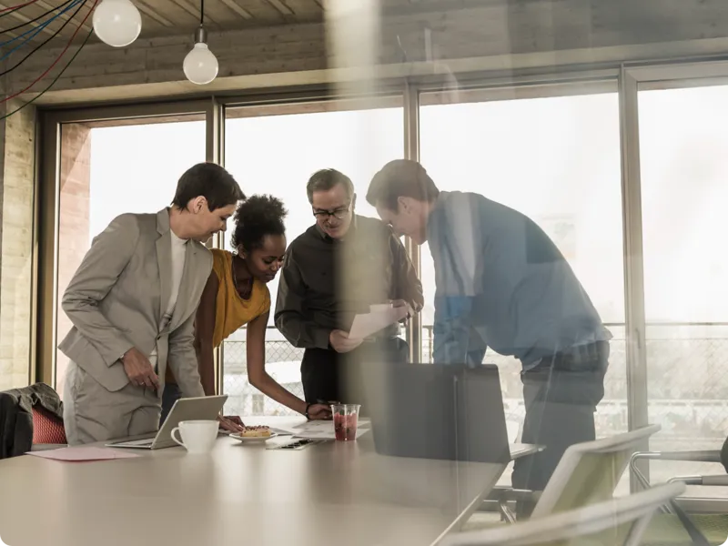 A group of people gather to look at a document in a sunny conference room