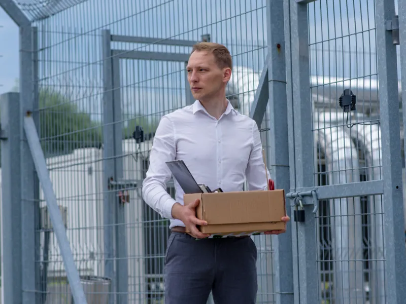 Person walking through large gates, holding a cardboard box.