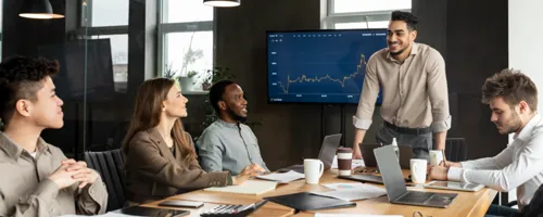 Agency meeting discussing a chart shown on a big screen TV.