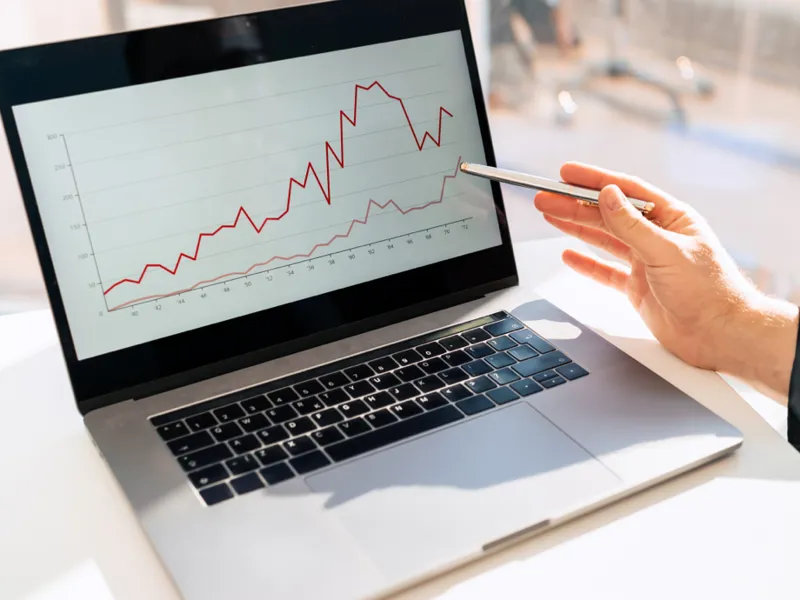 A person uses a pen to point to a graph on a laptop computer