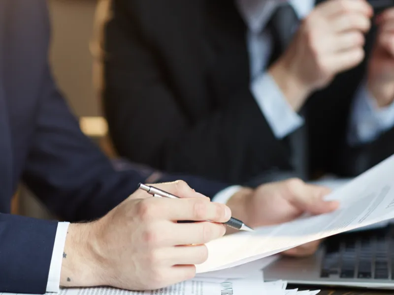 A person holds a pen up to a document as they study it.