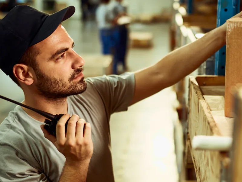 Factory worker wearing a black baseball cap, holding a CB radio.