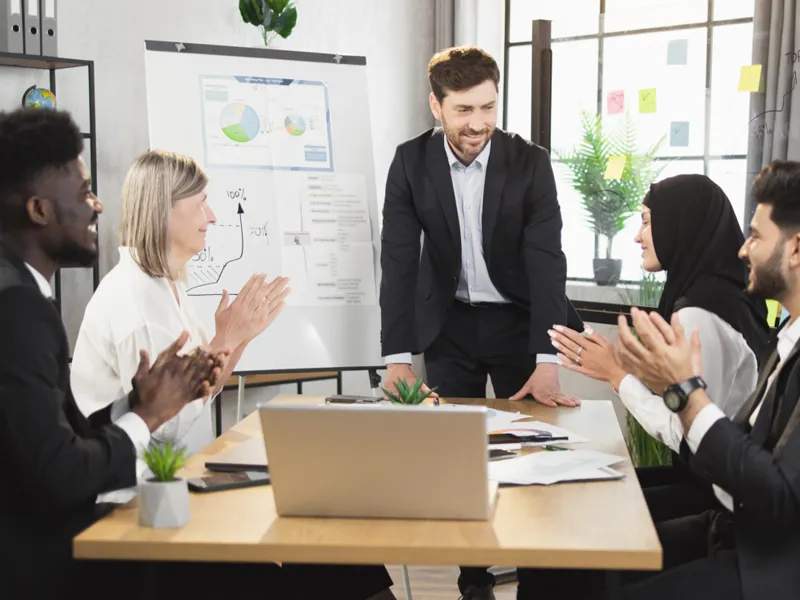 A diverse group of people clap for a presentation around a conference table