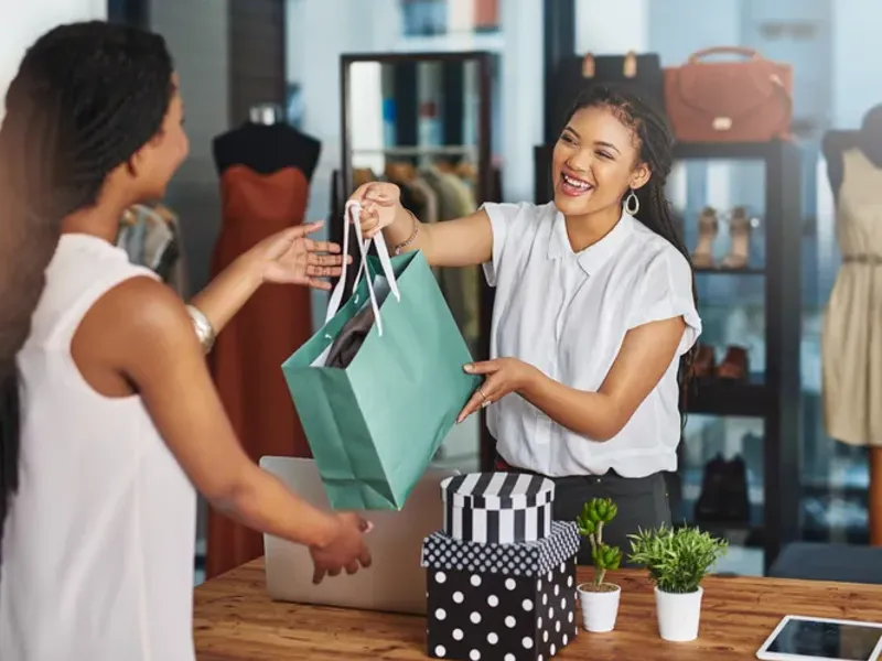 Smiling store employee handing shopping bags to customer.