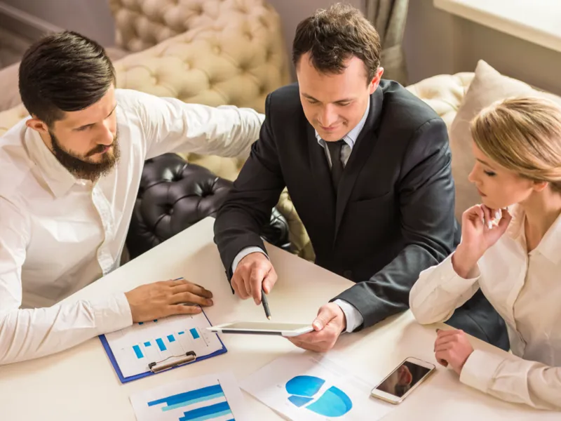 Three people conducting a meeting, seated at a table, looking at graphs and charts.
