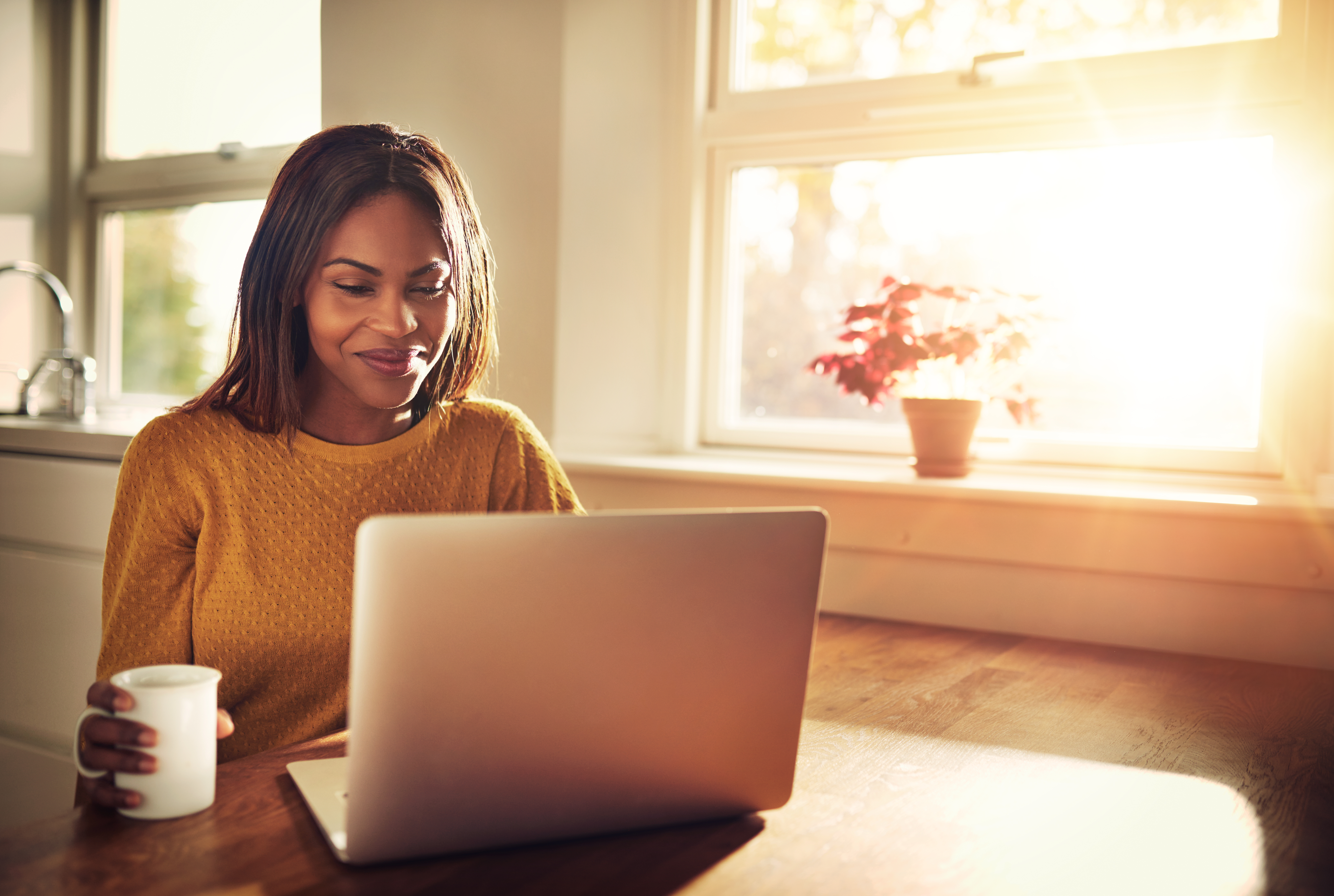 Smiling woman having coffee sitting on her laptop.